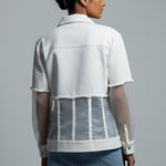 Woman wearing a white sheer jacket over a white shirt with denim shorts on a gray background