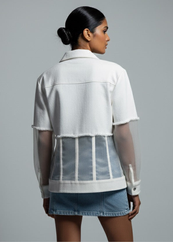 Woman wearing a white sheer jacket over a white shirt with denim shorts on a gray background