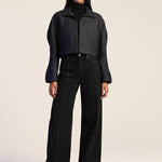 Woman wearing a black outfit with a jacket and pants on a plain background