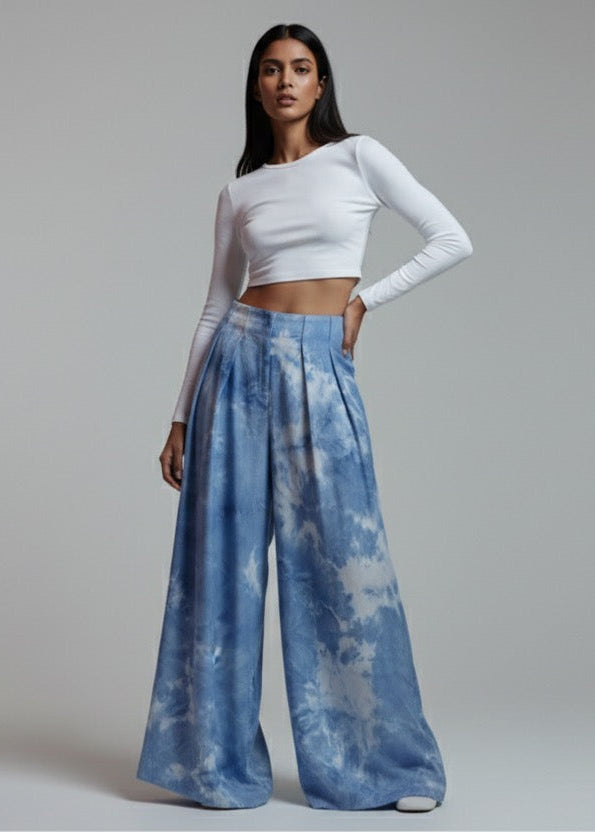 Woman wearing a white long-sleeve top and blue tie-dye pants on a gray background