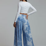 Woman wearing a white long-sleeve top and blue tie-dye pants on a plain background