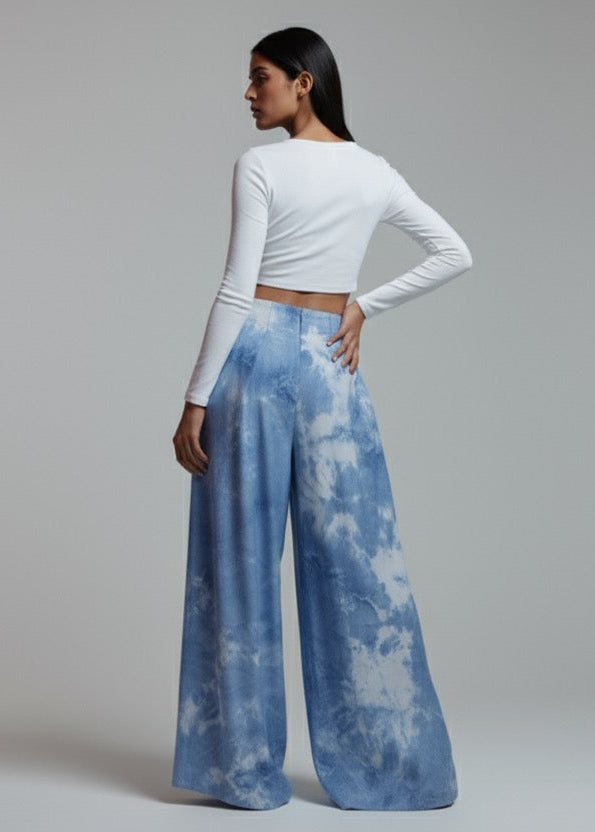 Woman wearing a white long-sleeve top and blue tie-dye pants on a plain background