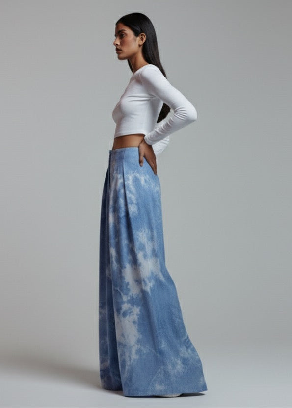 Woman wearing a white long-sleeve top and blue tie-dye pants on a plain background