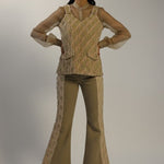 Woman wearing a beige knitted top and flared pants on a plain background