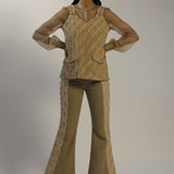 Woman wearing a beige knitted top and flared pants on a plain background