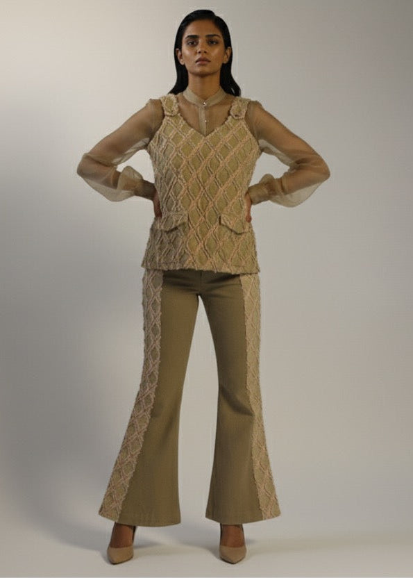 Woman wearing a beige knitted top and flared pants on a plain background
