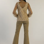 Woman wearing a patterned top and beige flared pants on a plain background
