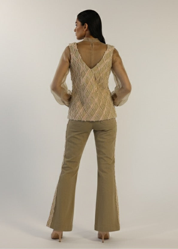 Woman wearing a patterned top and beige flared pants on a plain background