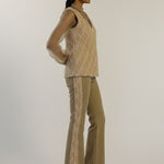 Woman wearing a beige knitted top and flared pants on a white background