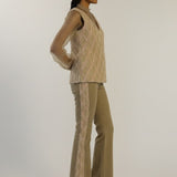 Woman wearing a beige knitted top and flared pants on a white background