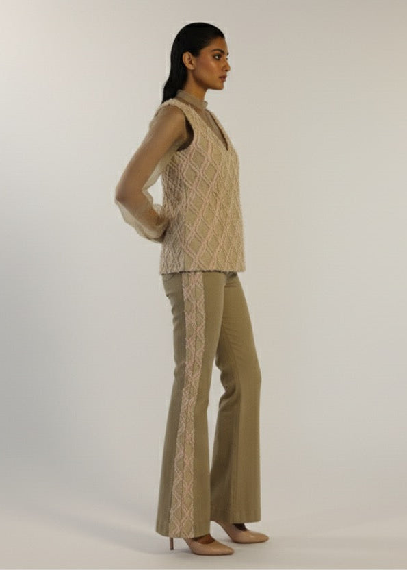 Woman wearing a beige knitted top and flared pants on a white background