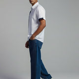Man wearing a white polo shirt and blue jeans standing against a plain background