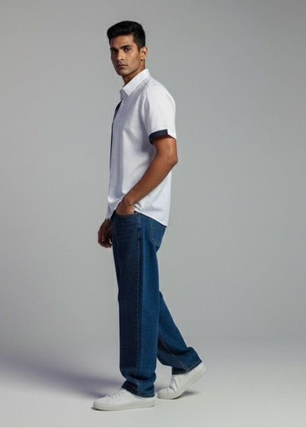 Man wearing a white polo shirt and blue jeans standing against a plain background
