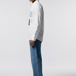 Man wearing a white shirt and blue jeans standing against a plain background
