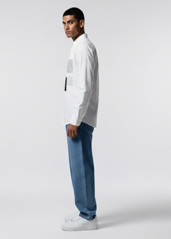 Man wearing a white shirt and blue jeans standing against a plain background
