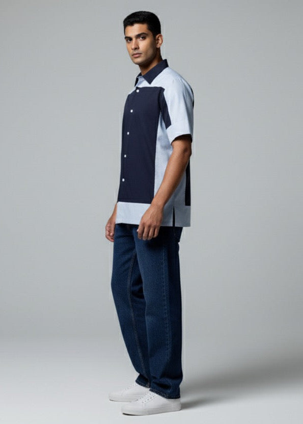 Man wearing a navy and white shirt with dark pants on a gray background