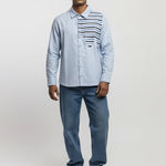 Man wearing a light blue shirt with a patterned vest, jeans, and white sneakers on a white background