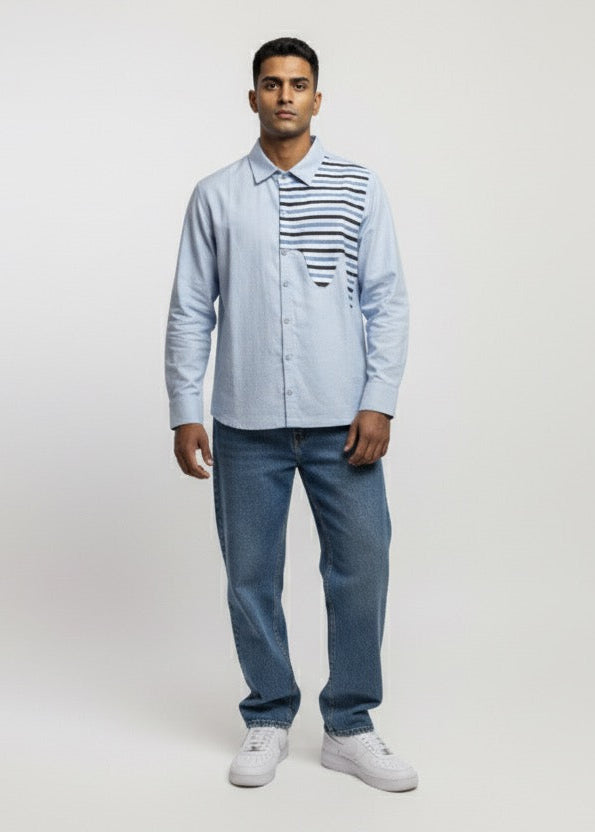 Man wearing a light blue shirt with a patterned vest, jeans, and white sneakers on a white background
