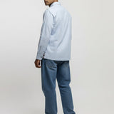 Man wearing a light blue shirt and jeans standing against a white background