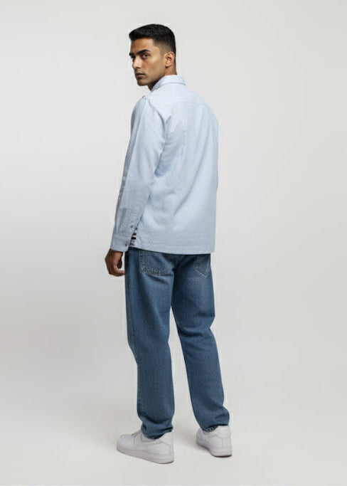Man wearing a light blue shirt and jeans standing against a white background