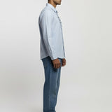 Man wearing a light blue shirt and jeans standing against a white background