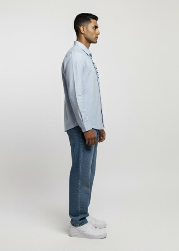 Man wearing a light blue shirt and jeans standing against a white background