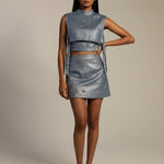 Woman wearing a metallic silver sleeveless top and skirt set on a beige background