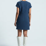 Woman wearing a blue dress and white boots on a light gray background