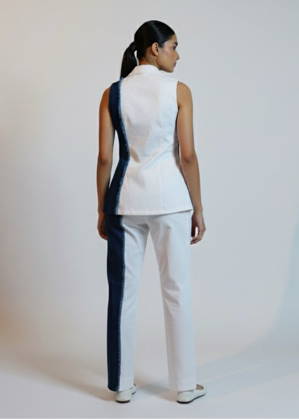 Woman wearing a white sleeveless top and pants with black stripes on a plain background