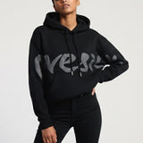 Person wearing a black hoodie with 'Versace' branding on a light gray background