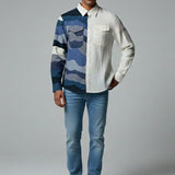 Man wearing a patterned shirt and jeans on a plain background