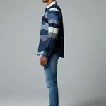 Man wearing a blue plaid shirt and jeans standing against a gray background