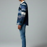 Man wearing a blue plaid shirt and jeans standing against a gray background