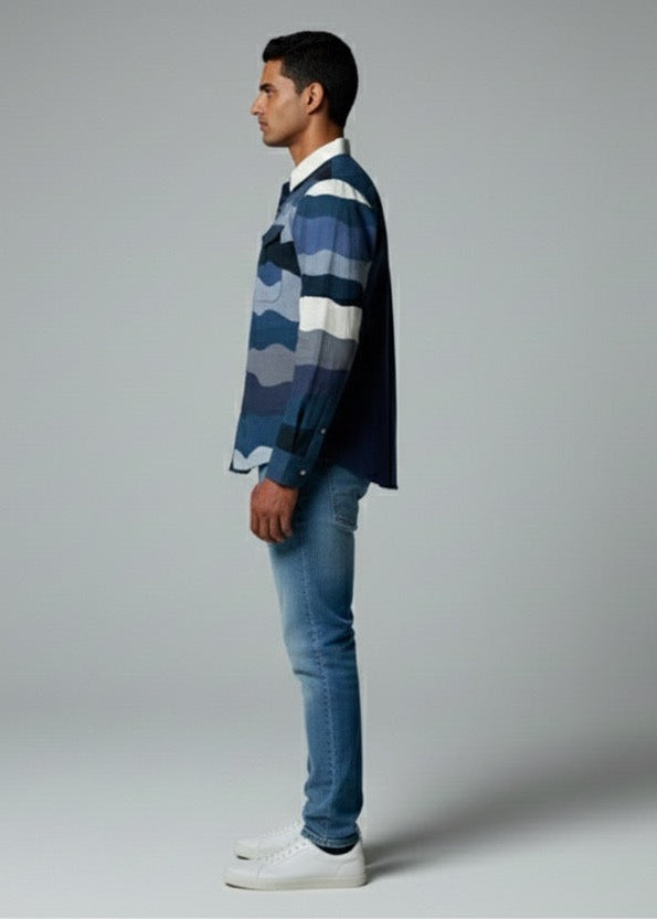 Man wearing a blue plaid shirt and jeans standing against a gray background