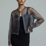 Woman wearing a sheer black jacket over a black dress on a gray background