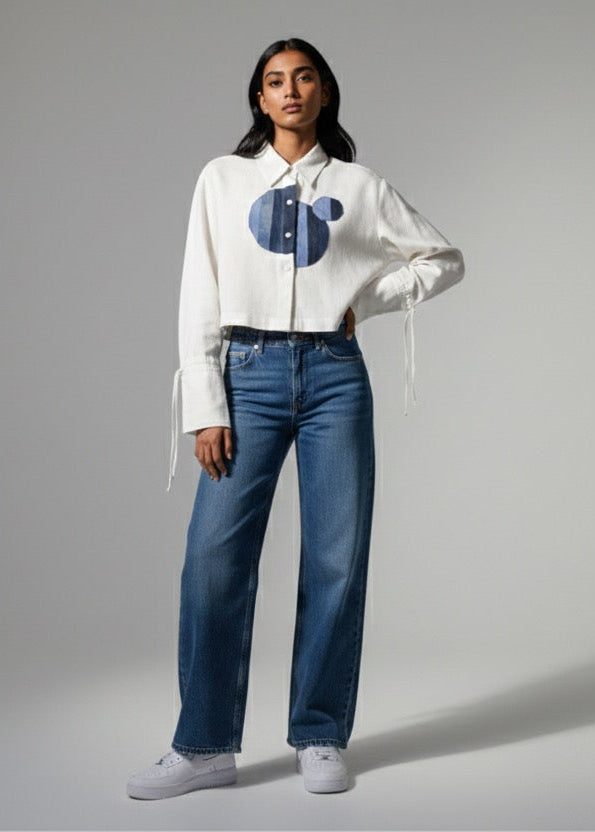 Woman wearing a white blouse with a blue design and blue jeans on a gray background