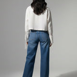 Person wearing a white shirt and blue jeans standing against a gray background