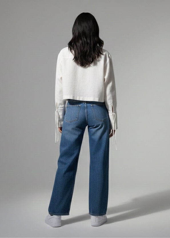 Person wearing a white shirt and blue jeans standing against a gray background
