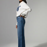 Woman wearing a white sweater and blue jeans on a gray background