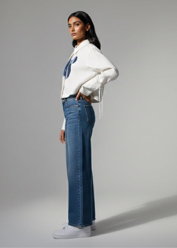 Woman wearing a white sweater and blue jeans on a gray background