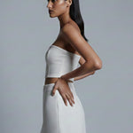 Woman wearing a white strapless top and skirt against a gray background