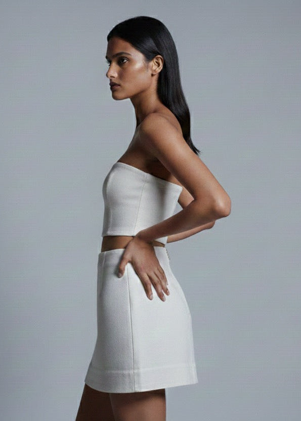 Woman wearing a white strapless top and skirt against a gray background