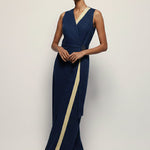 Woman wearing a navy evening gown with a gold stripe on a plain background