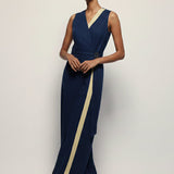 Woman wearing a navy evening gown with a gold stripe on a plain background