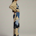 Woman wearing a beige sweater and patterned pants on a plain background