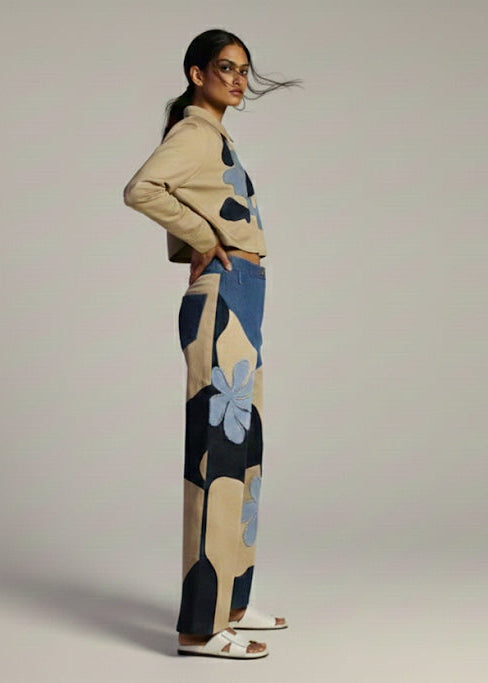 Woman wearing a beige sweater and patterned pants on a plain background