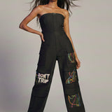 Woman wearing a black strapless jumpsuit with colorful designs on a plain background