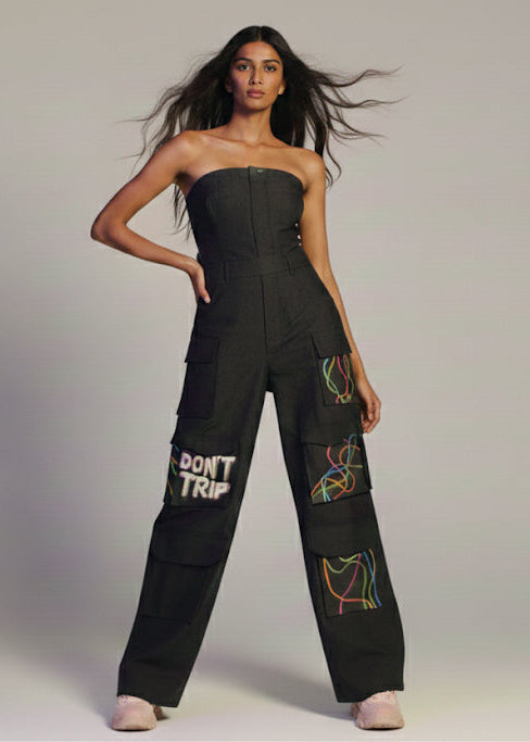 Woman wearing a black strapless jumpsuit with colorful designs on a plain background