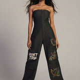 Woman wearing a black jumpsuit with text and patterns on a plain background