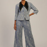 Woman wearing a denim suit with black accents on a plain background